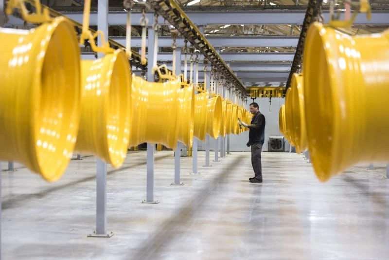Factory worker inspecting yellow industrial pipes on a conveyor belt.